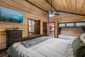 Ein Interieur einer Holzhütte mit einem großen Bett, einem Deckenventilator und einem Gemälde einer Waldlandschaft.