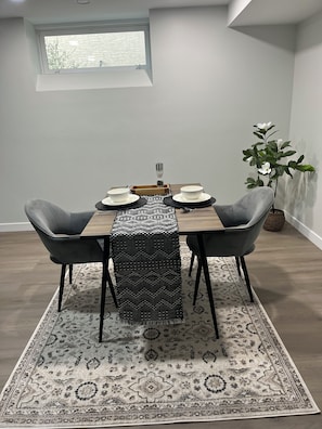 Ein Essbereich mit einem Tisch für zwei Personen, einem gemusterten Teppich und einem Blumentopf.