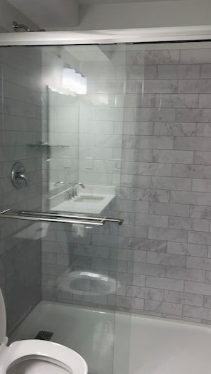 Ein Badezimmer mit einer gläsernen Duschkabine, einer weißen Toilette und einer gefliesten Wand.