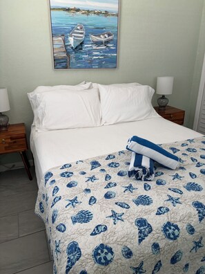 A bedroom with a bed, a nightstand, a lamp, and a painting of boats on the wall.