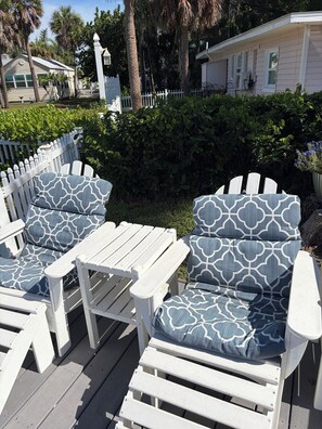 Outdoor furniture with patterned cushions, a white picket fence, and a residential building in the background.