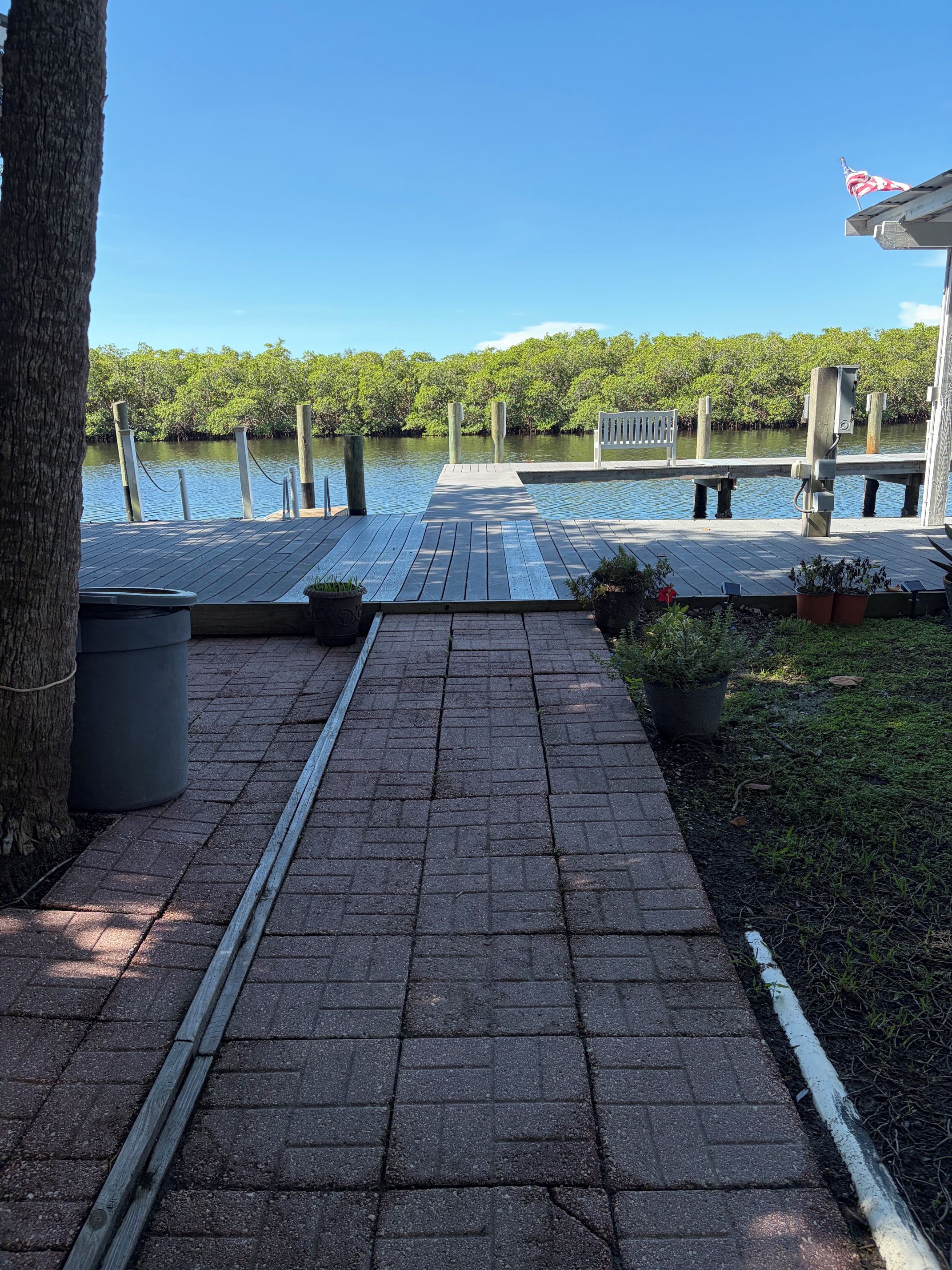 A wooden dock leading to a calm body of water, surrounded by greenery and a clear sky.