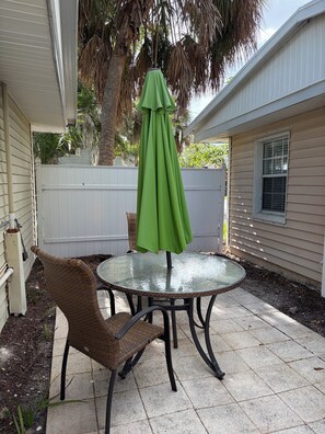 A patio with a round glass table and chairs, a green umbrella, and a white fence. - Cozy 2-bedroom cottage in Ruskin. (Ruskin)