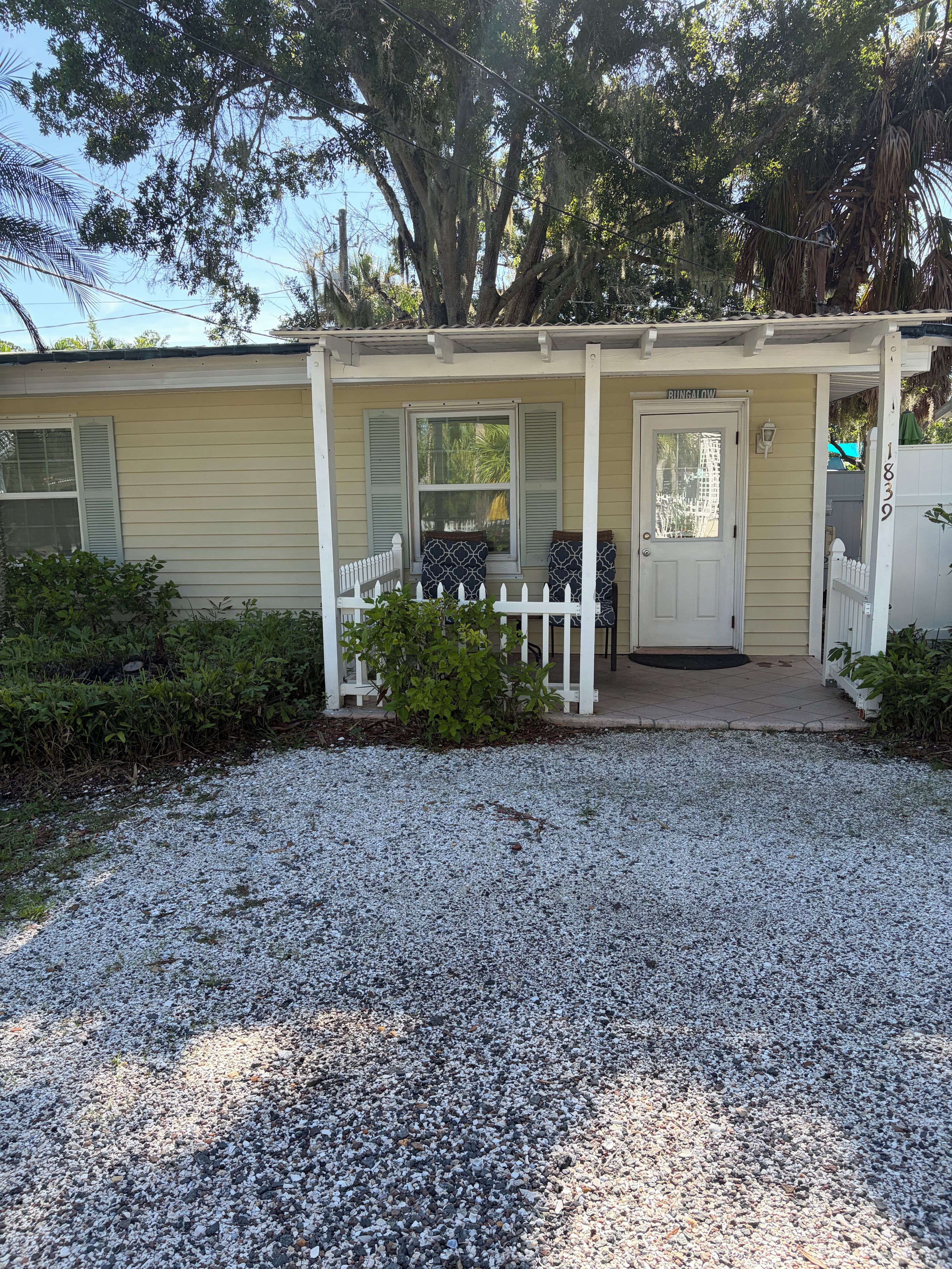 A bungalow with a porch, a white picket fence, and a gravel driveway.