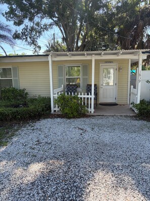 A bungalow with a porch, a white picket fence, and a gravel driveway. - Cozy 2-bedroom cottage in Ruskin. (Ruskin)