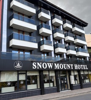 Ein mehrstöckiges Hotel mit Balkonen, einer gut sichtbaren Beschilderung mit dem Schriftzug 'Snow Mount Hotel' und einem Logo, das es als Hotel und Spa kennzeichnet.