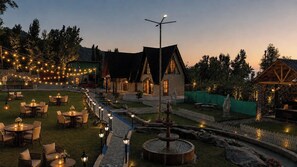 An outdoor dining area with tables and chairs, a fountain, and string lights. - Avora Mountain Resort  (Gund)