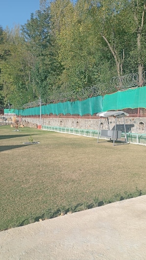 Un espacio al aire libre con un campo cubierto de césped, un muro de piedra y una cerca verde de malla.