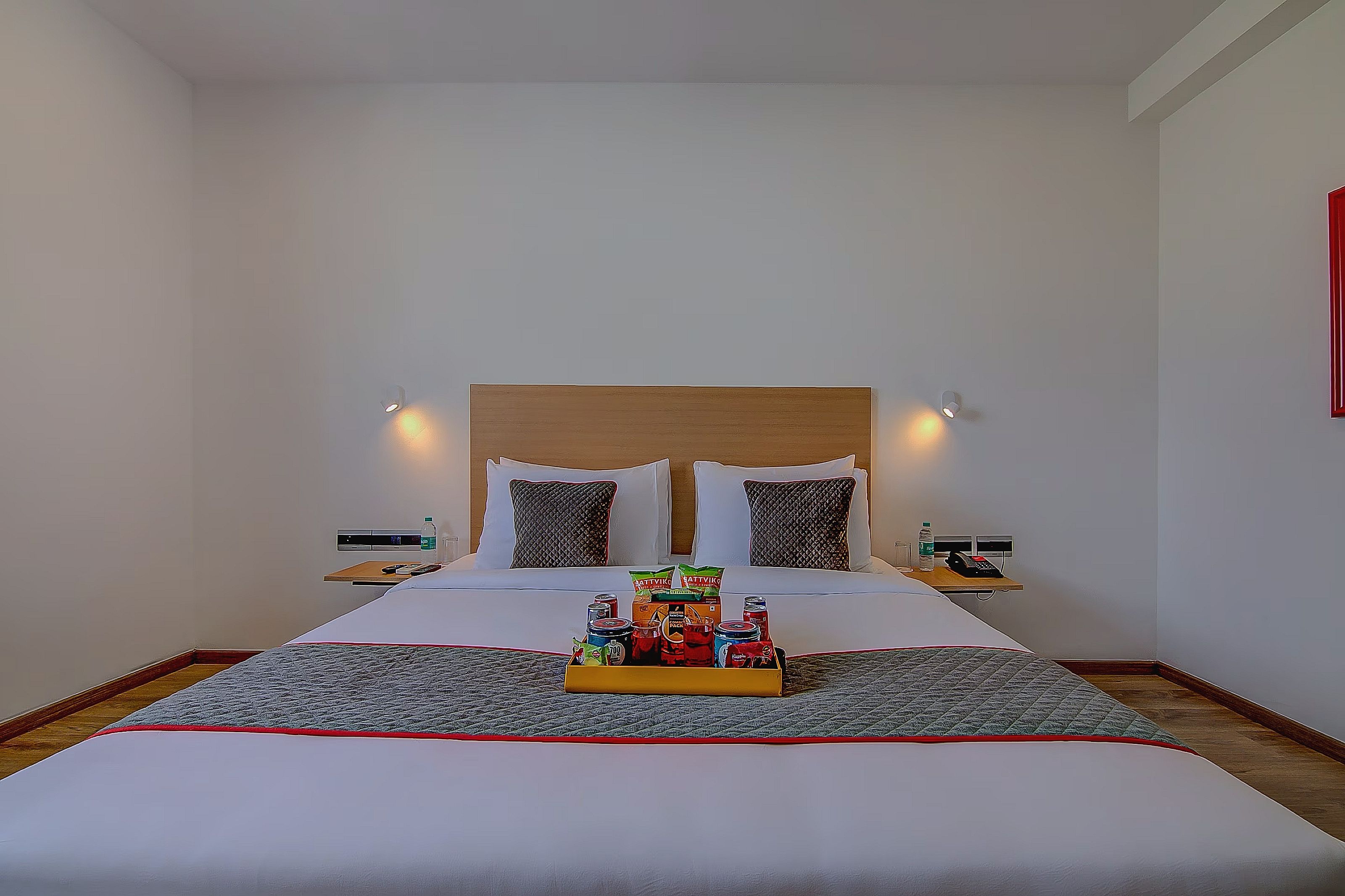 Habitación de hotel con una cama grande, dos mesitas de noche, un cabecero y una bandeja de aperitivos.