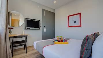 A hotel room with a bed, a desk, a chair, a TV, a door, and a framed picture on the wall.