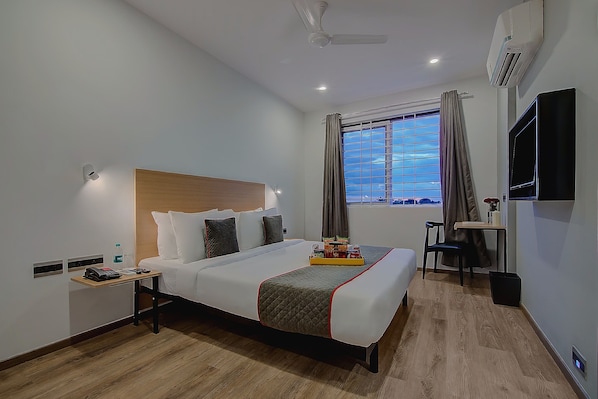 Quarto de hotel com cama, mesa de cabeceira, janela e escrivaninha com cadeira.