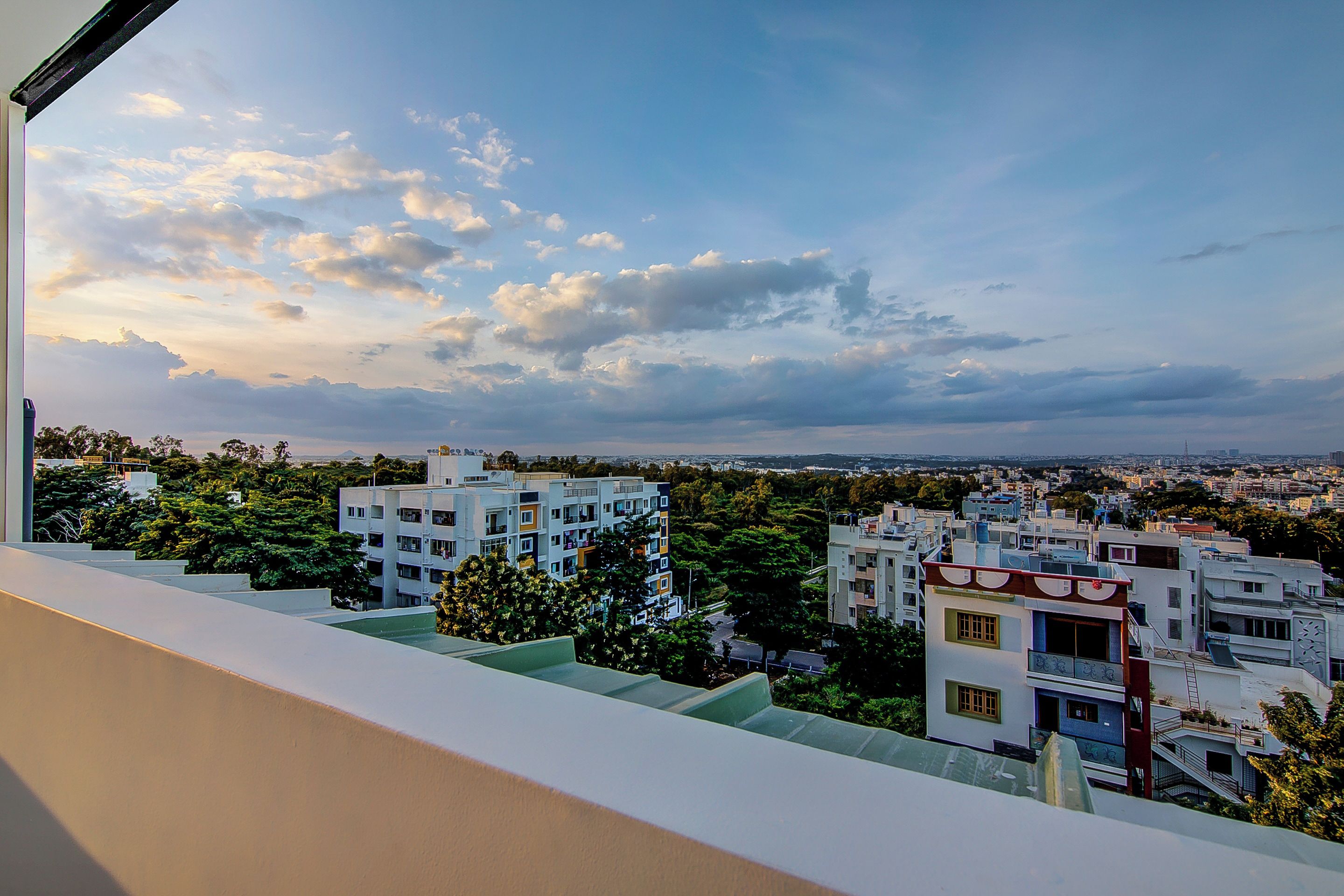 A residential area with multi-story buildings, a clear sky with clouds, and a distant view of a cityscape.