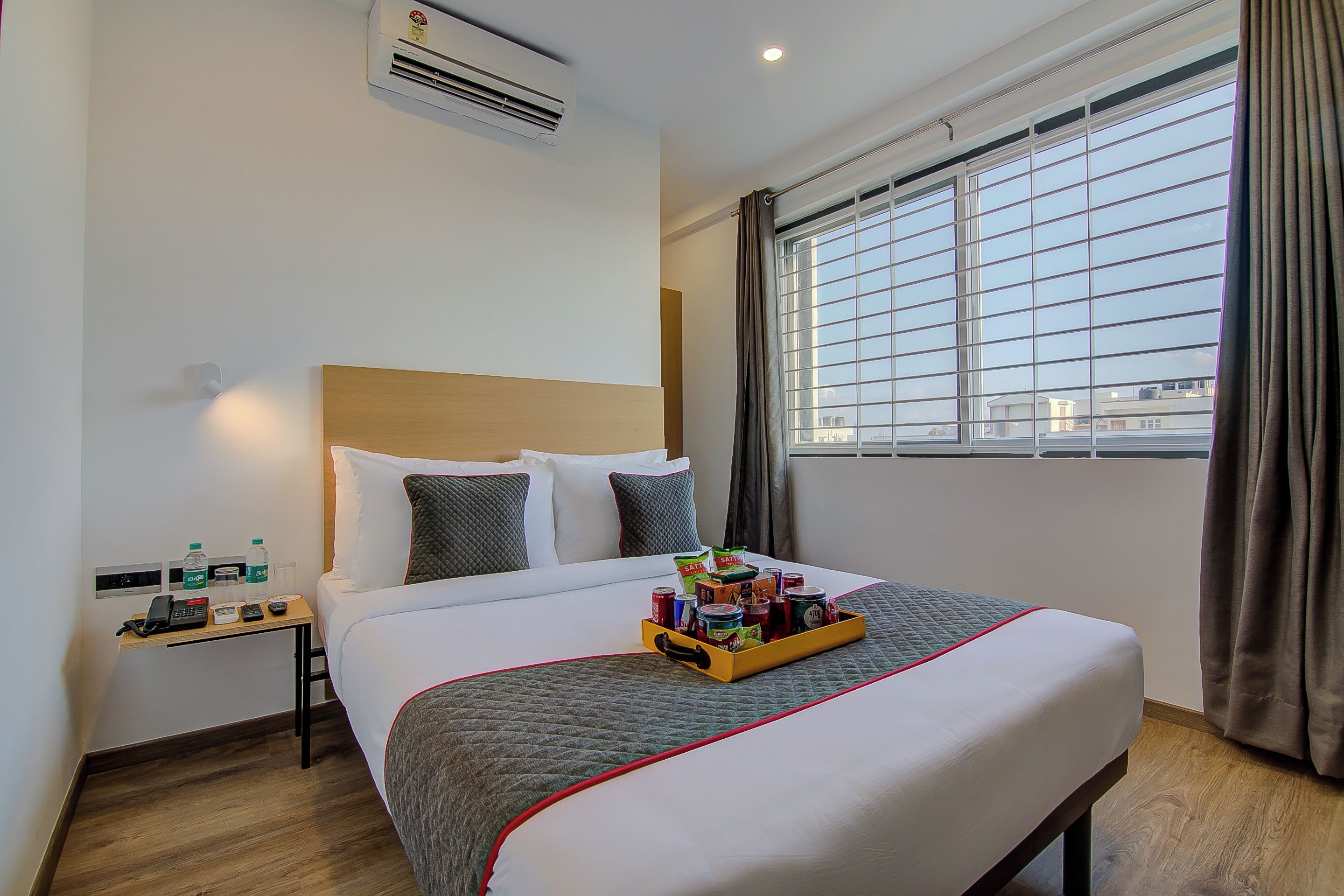 Una habitación de hotel con cama, mesita de noche y ventana con cortinas.