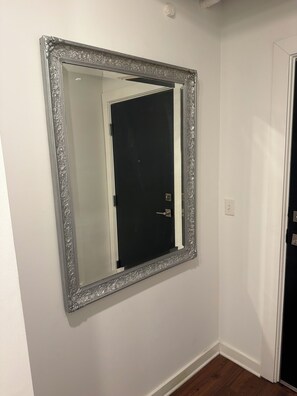 Een grote spiegel met een sierlijk zilveren frame, bevestigd aan een effen witte muur.