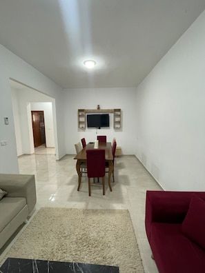 A dining area with a table and chairs, a flat-screen TV mounted on the wall, a red sofa, and a marble-tiled floor. - Villa Lina, Djerba, Midoun (Djerba Midun)