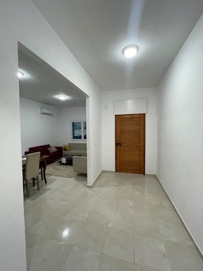 A hallway with a wooden door, a dining area with a table and chairs, and a living area with a sofa and a TV. - Villa Lina, Djerba, Midoun (Djerba Midun)