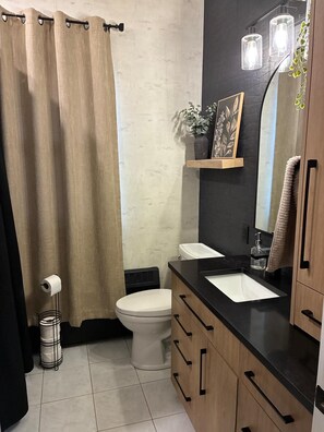 A bathroom with a toilet, sink, and shower curtain. - Cozy & Stylish Leamington Retreat / Fireplace, Modern Comfort & Prime Location (Leamington)