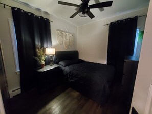 A bedroom with a bed, a nightstand with a lamp, a ceiling fan, and a macrame wall hanging. - Cozy & Stylish Leamington Retreat / Fireplace, Modern Comfort & Prime Location (Leamington)