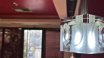 Un interior moderno con una lámpara colgante de cristal transparente, una pared roja y vistas a un comedor con sillas y una mesa.