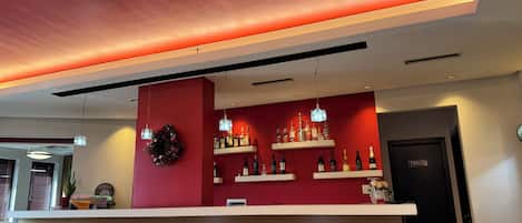 A reception area with a red wall, a white reception desk, and shelves of bottled beverages.