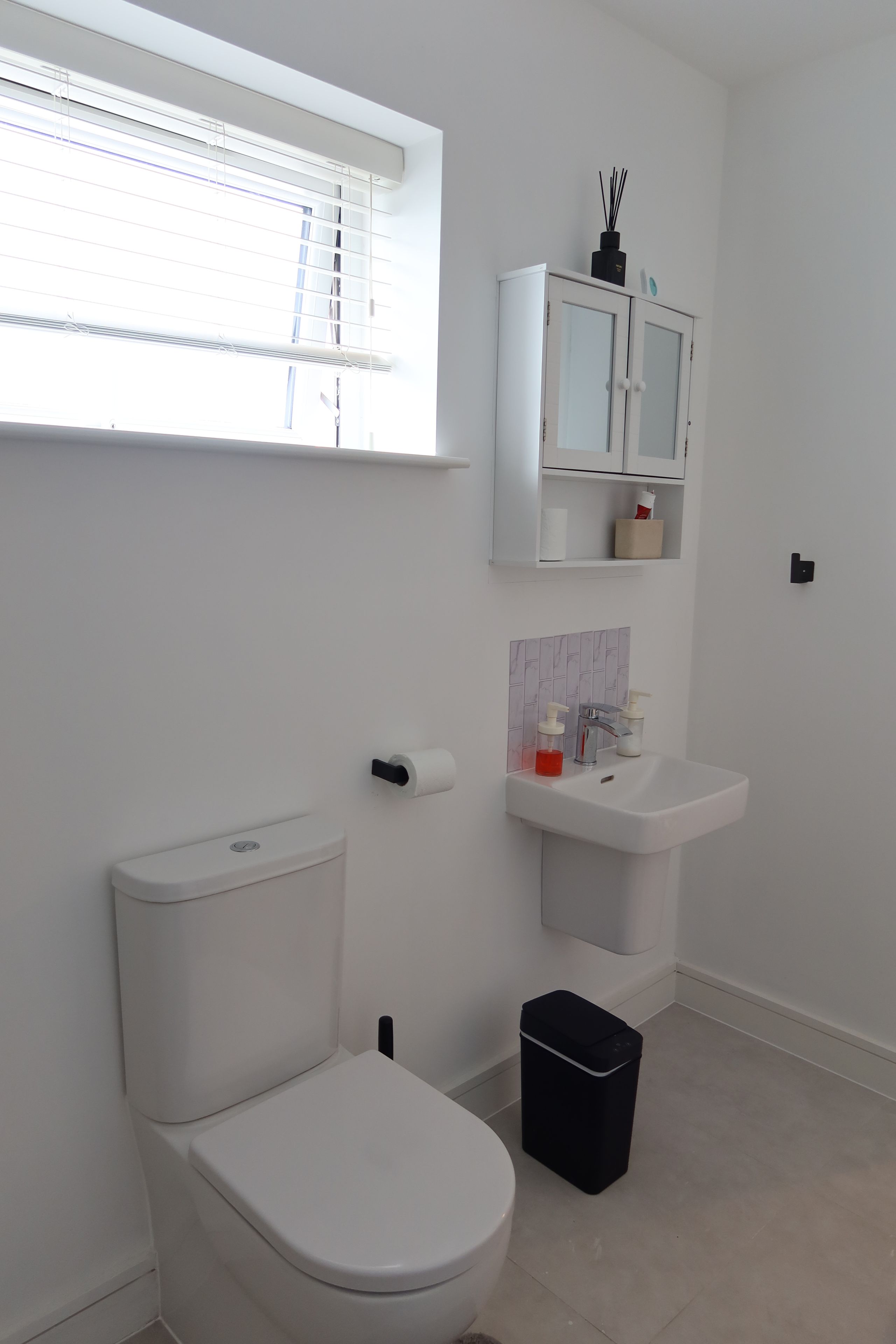 Ein modernes Badezimmer mit Toilette, Waschbecken, einem Schrank und einem Fenster.