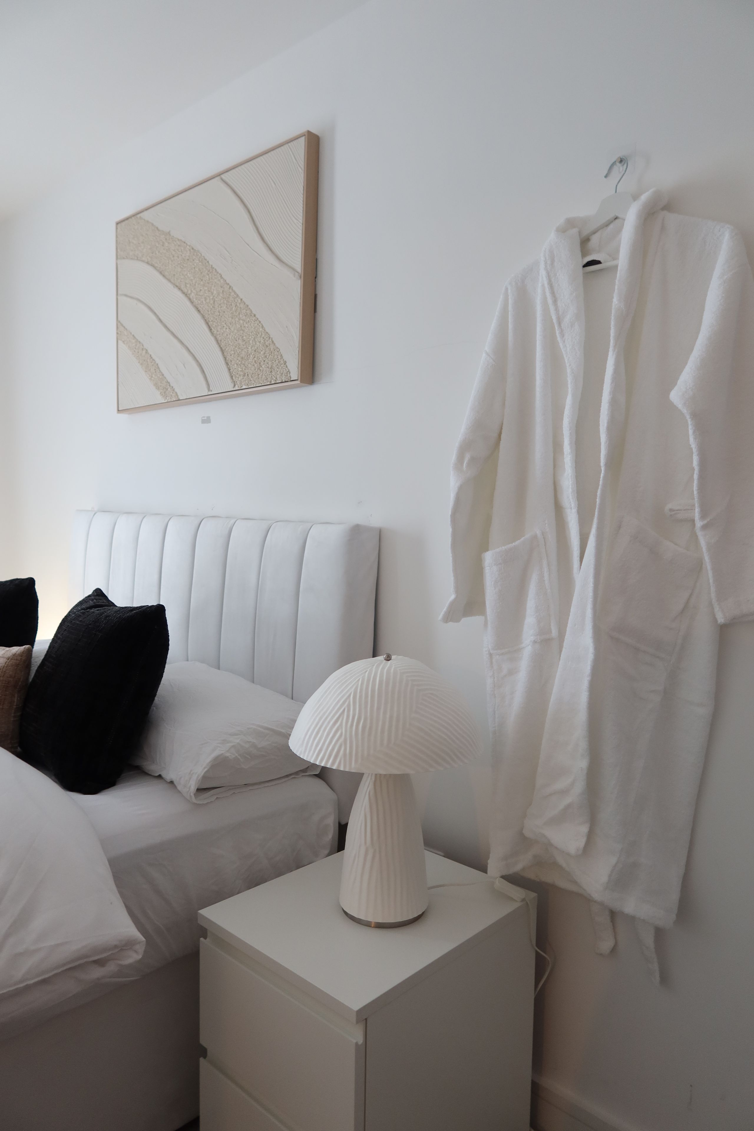 Una camera da letto con un letto, un comodino con una lampada, un appendiabiti e un quadro astratto appeso al muro.