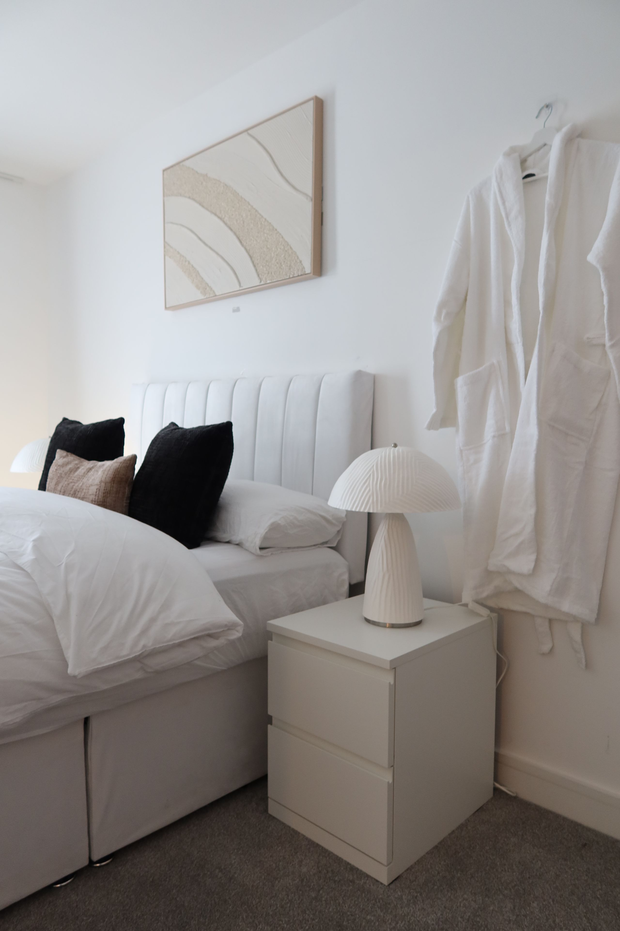 Une chambre à coucher au style minimaliste, avec un lit, une table de chevet, une lampe et un porte-vêtements suspendu.