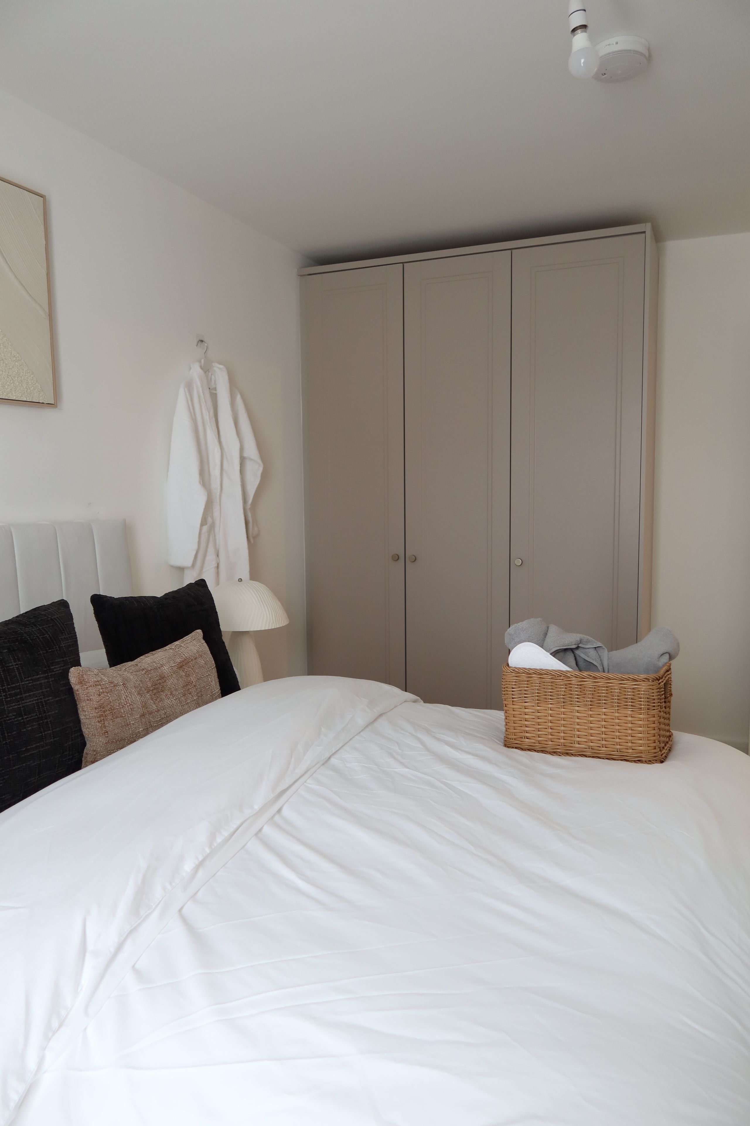 A bedroom with a large bed, a wardrobe, a hanging robe, and a basket of towels.