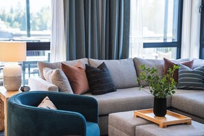 A modern living room with a sofa, a blue armchair, a wooden side table, and a potted plant. - 2 Turns by Revelstoke Vacations (Revelstoke)