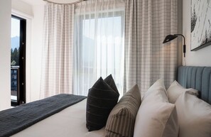 A bedroom with a bed, pillows, a bedside table, a lamp, and a window with curtains. - 2 Turns by Revelstoke Vacations (Revelstoke)
