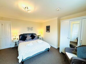 Ein Hotelzimmer mit einem Bett, zwei Nachttischen mit Lampen, einem Sessel, einem Bild an der Wand und einer Tür.