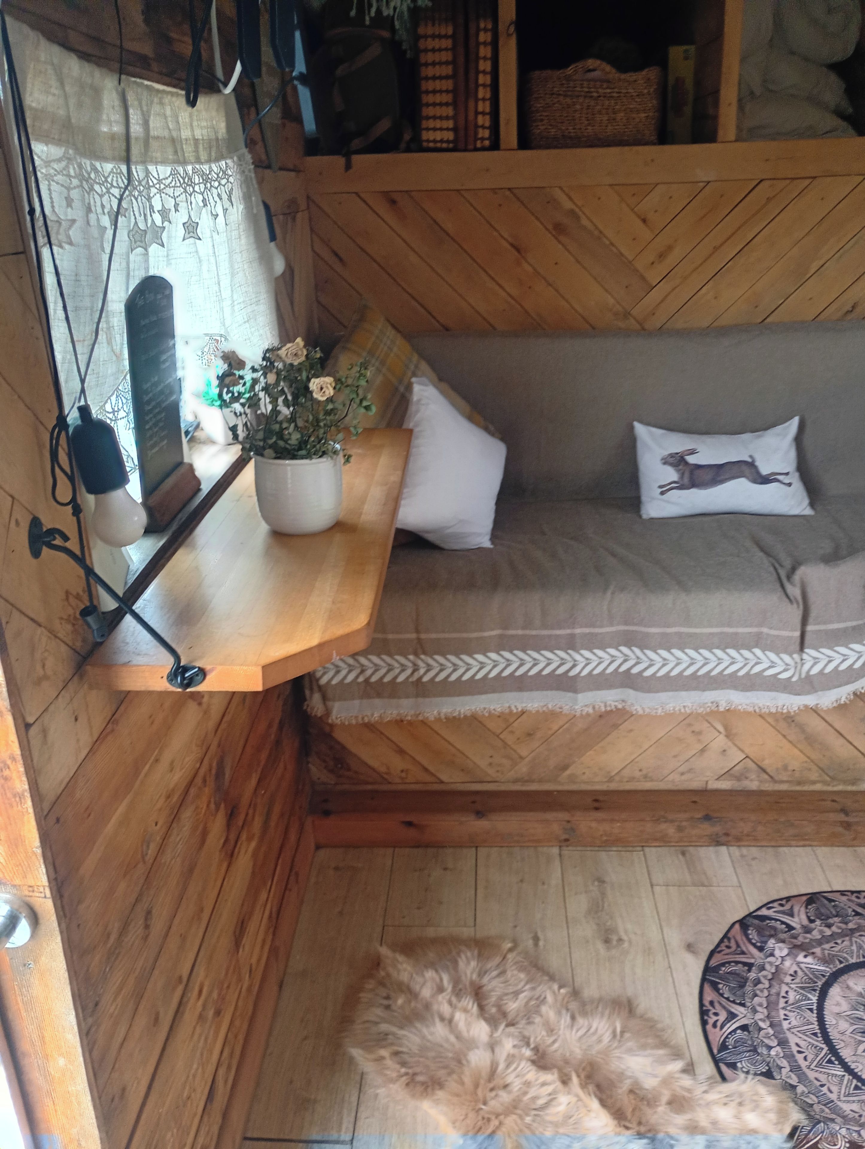 A cozy room with a wooden bench, a small table with a potted plant, a fluffy rug, and a patterned throw on the floor.
