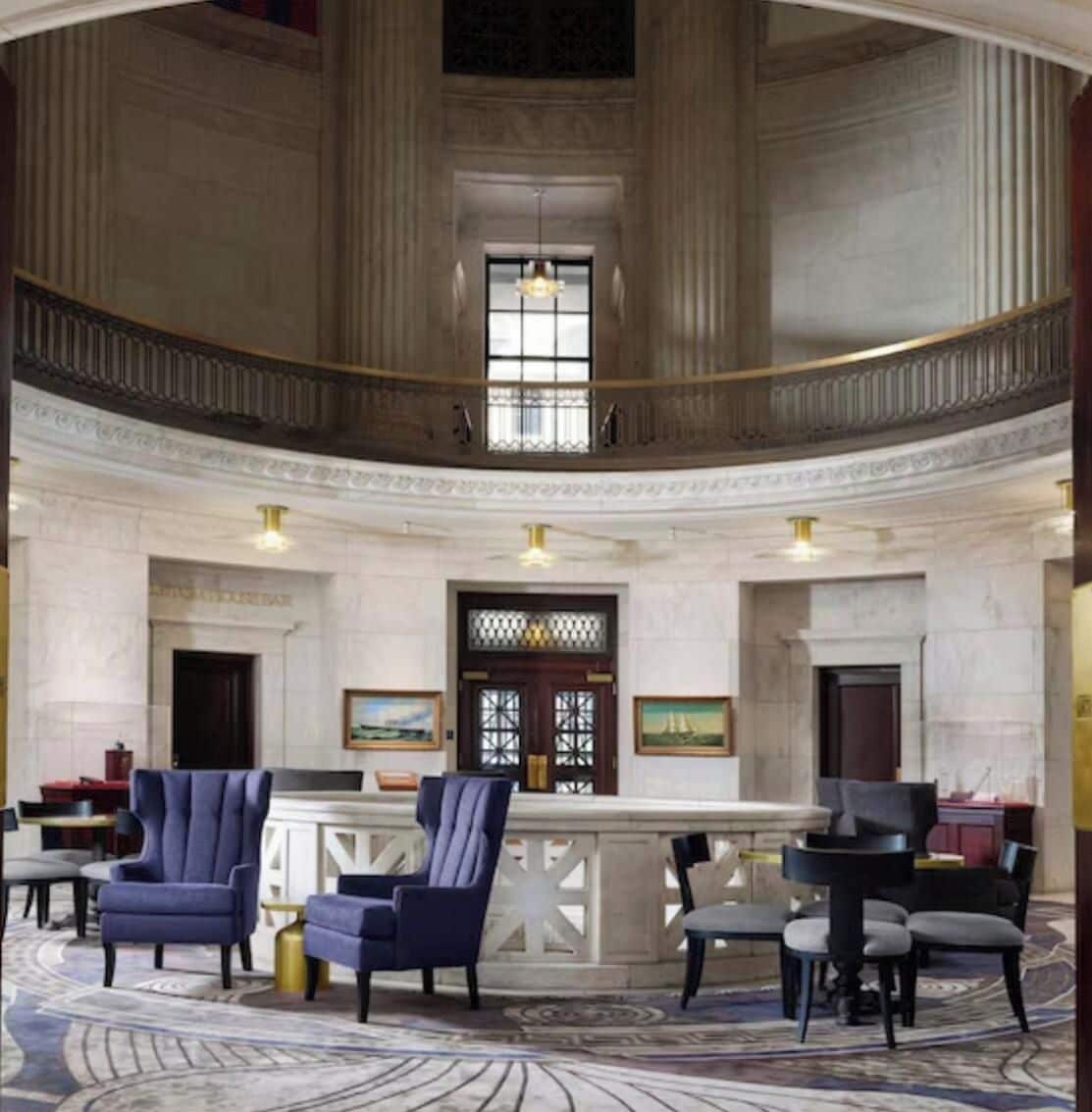 A grand lobby with a high ceiling, a central staircase, and a reception desk.