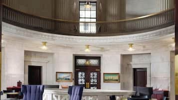 A grand lobby with a high ceiling, a central staircase, and a reception desk.