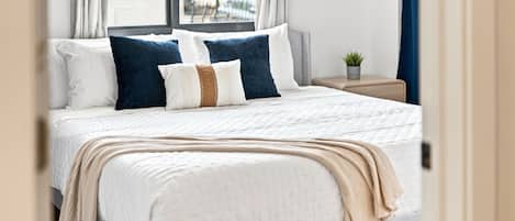 Ein ordentlich bezogenes Bett mit weißer Daunendecke, zwei Kissen und einer beige farbenen Tagesdecke.