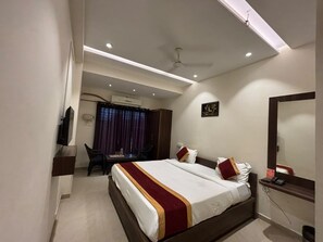 Ein Hotelzimmer mit einem großen Bett, einem Schreibtisch, einem Sessel, einem Fernseher und einem Deckenventilator.