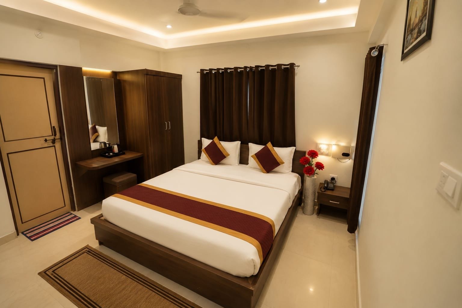 Una habitación de hotel con una cama grande, un armario, una mesita de noche con lámpara y otra mesita auxiliar.