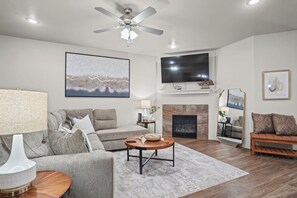 A living room with a sofa, coffee table, TV, fireplace, and artwork. - Six Gun's Up - 3BR/3BA - Walk to Tech (Lubbock)