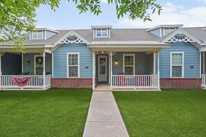 A two-story house with a covered porch, a brick foundation, and a well-maintained lawn. - Six Gun's Up - 3BR/3BA - Walk to Tech (Lubbock)