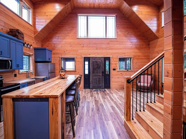 A wooden cabin interior with a kitchen, dining area, and a staircase.