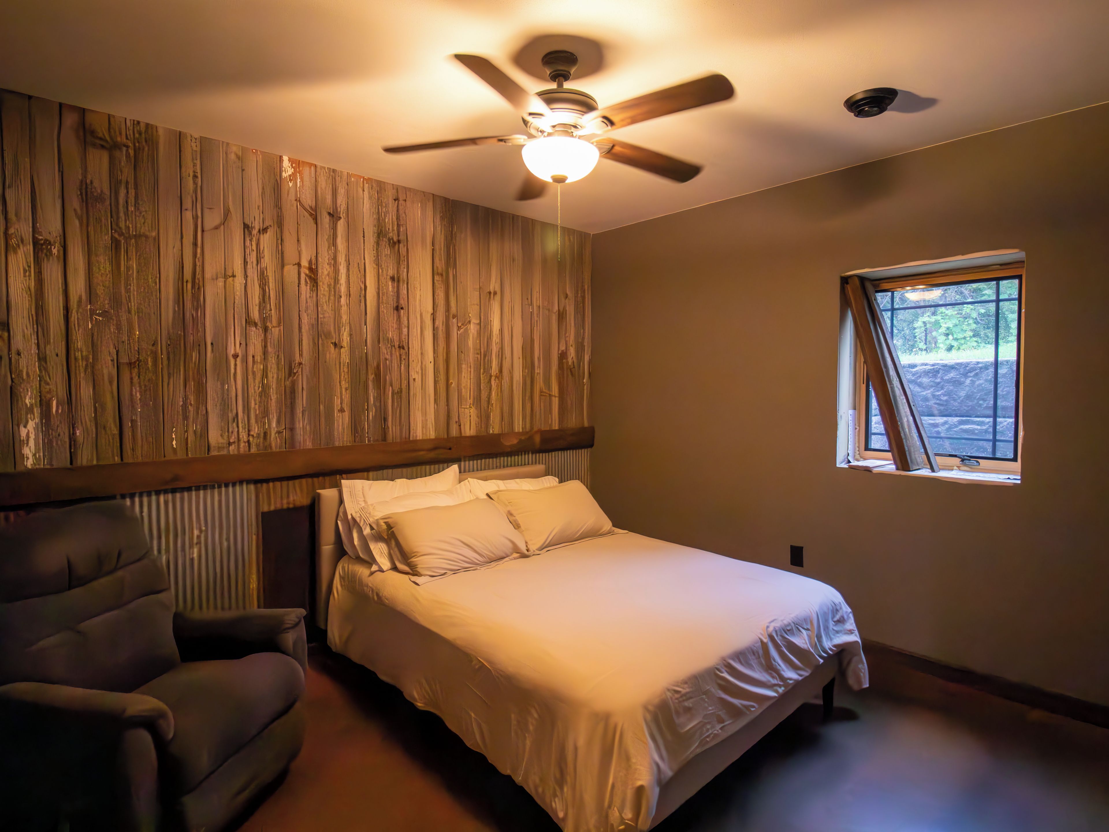 Une chambre à coucher avec un lit, une chaise, un ventilateur de plafond et une fenêtre.
