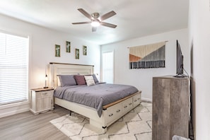 A bedroom with a bed, bedside tables, a ceiling fan, a wall-mounted TV, and a window with blinds. - Longhorn Landing, 10 mins to Zilker Park, ACL (Austin)