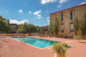 A swimming pool with a red-tiled deck, surrounded by outdoor furniture and a brick building. - Longhorn Landing, 10 mins to Zilker Park, ACL (Austin)
