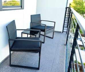 A balcony with two chairs and a table, a railing, and a view of greenery. - Oak Lawn 3BR Townhome | Private Yard & Pool Table (Dallas)