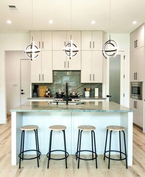 A modern kitchen with a central island, bar stools, and pendant lighting. - Oak Lawn 3BR Townhome | Private Yard & Pool Table (Dallas)