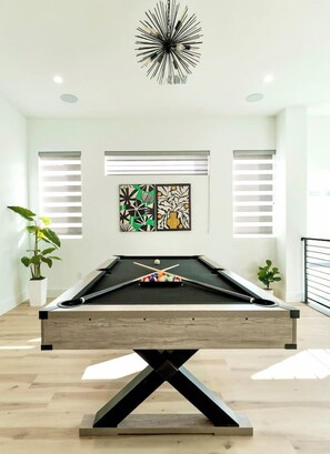 A pool table in a room with white walls, a ceiling light fixture, and two windows with blinds. - Oak Lawn 3BR Townhome | Private Yard & Pool Table (Dallas)