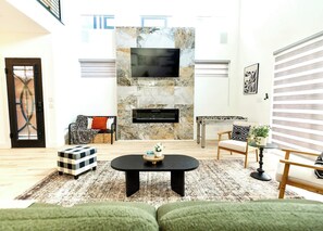 A living room with a fireplace, a television mounted above it, and a sofa. - Oak Lawn 3BR Townhome | Private Yard & Pool Table (Dallas)