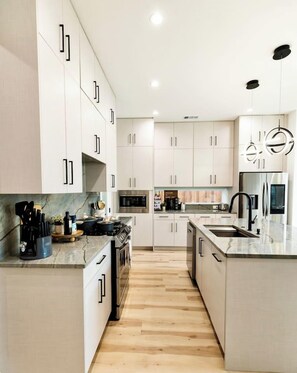 A modern kitchen with white cabinetry, a central island, stainless steel appliances, and a wooden floor. - Oak Lawn 3BR Townhome | Private Yard & Pool Table (Dallas)