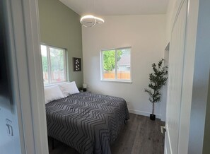 Una camera da letto con un letto, due finestre, una pianta in vaso e un lampadario.
