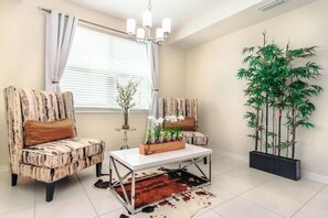 A living room with two patterned armchairs, a white coffee table, a potted plant, and a large bamboo plant. - Modern 2BR Condo Near Disney w/ Resort Amenities (Kissimmee)